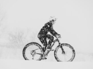 B&W photo or woman riding fat bike in a snowstorm.