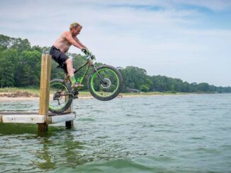 shirtless man on fat bike jumping off pier into lake